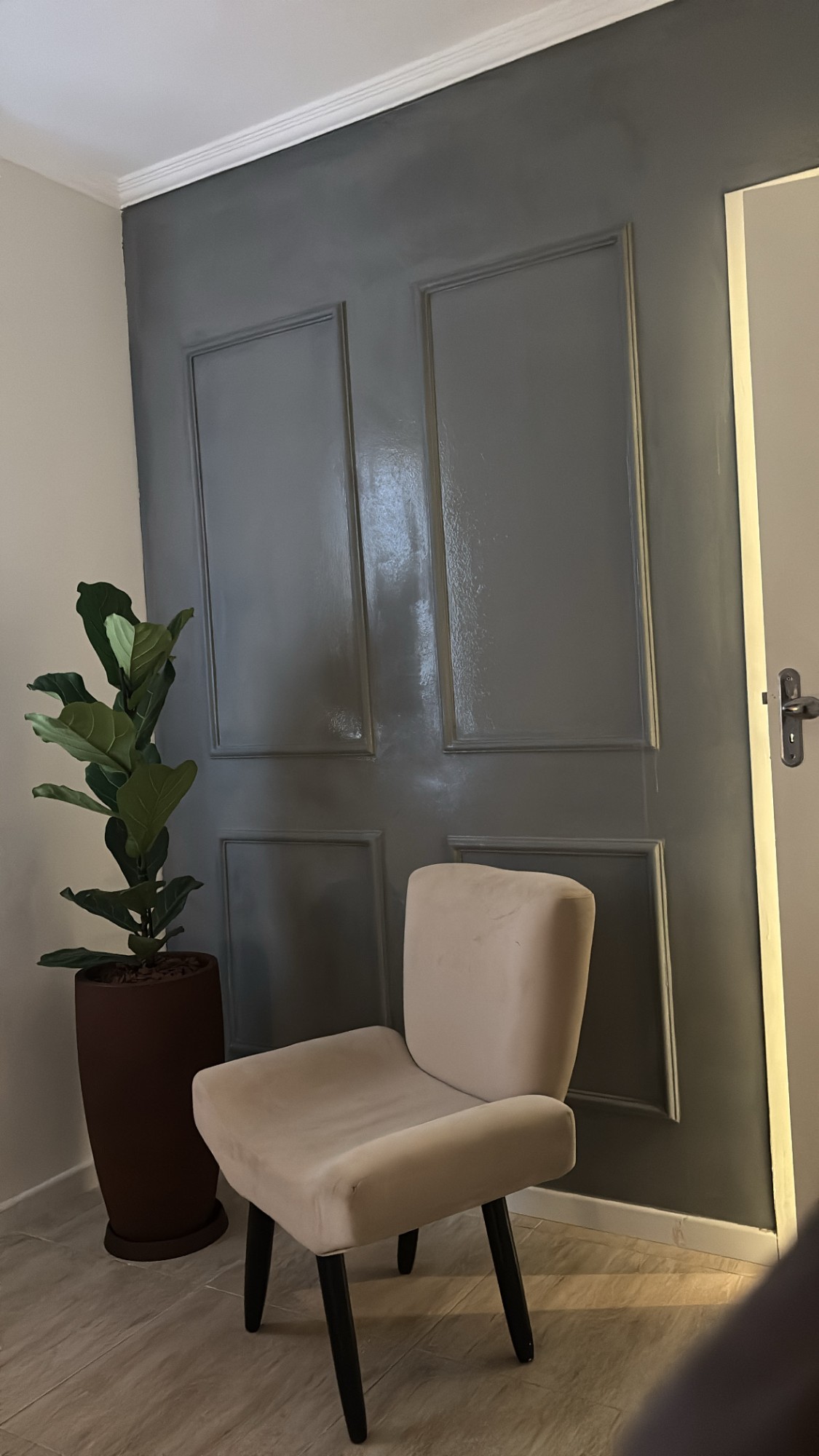 Sala de espera de consultório com poltrona clara, planta e parede escura
